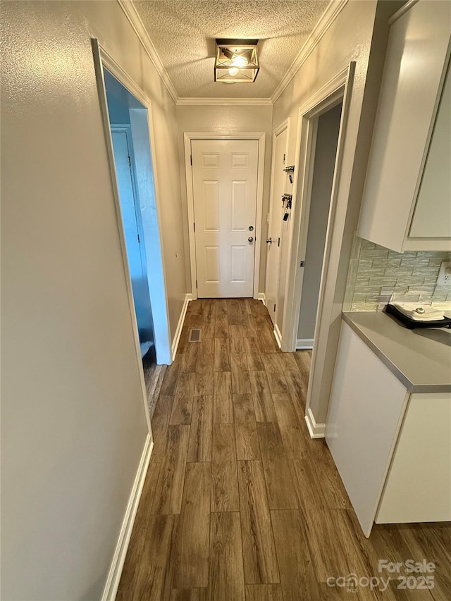 hall featuring dark wood-style floors, visible vents, crown molding, baseboards, and a textured ceiling