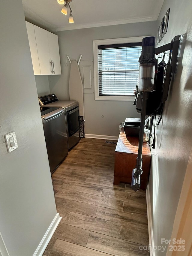 clothes washing area with wood finished floors, washing machine and dryer, crown molding, baseboards, and cabinet space