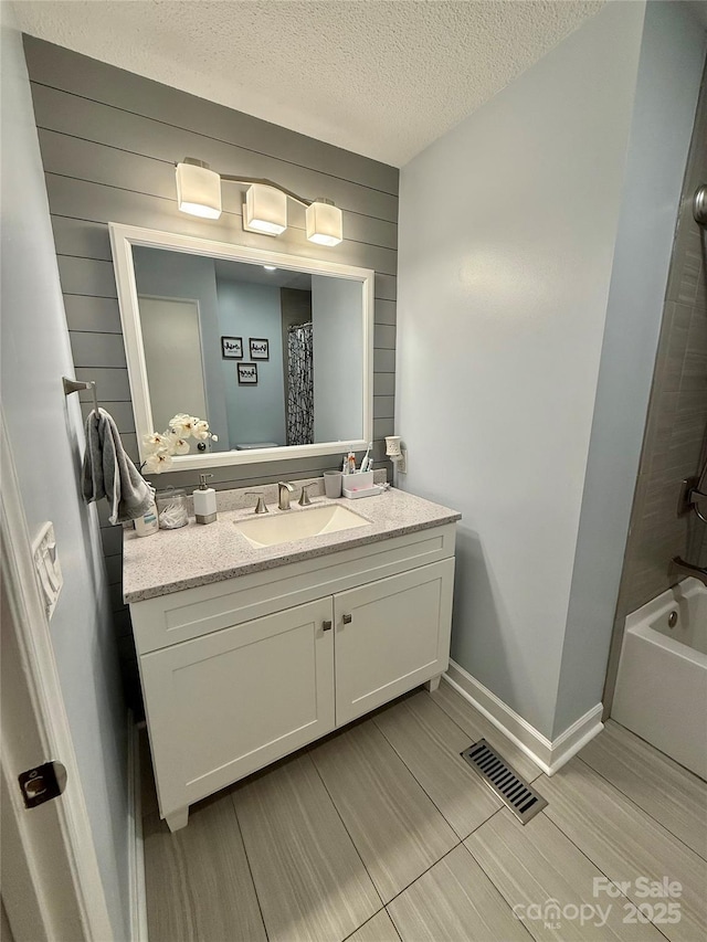 full bath featuring wood walls, visible vents, vanity, baseboards, and a textured ceiling