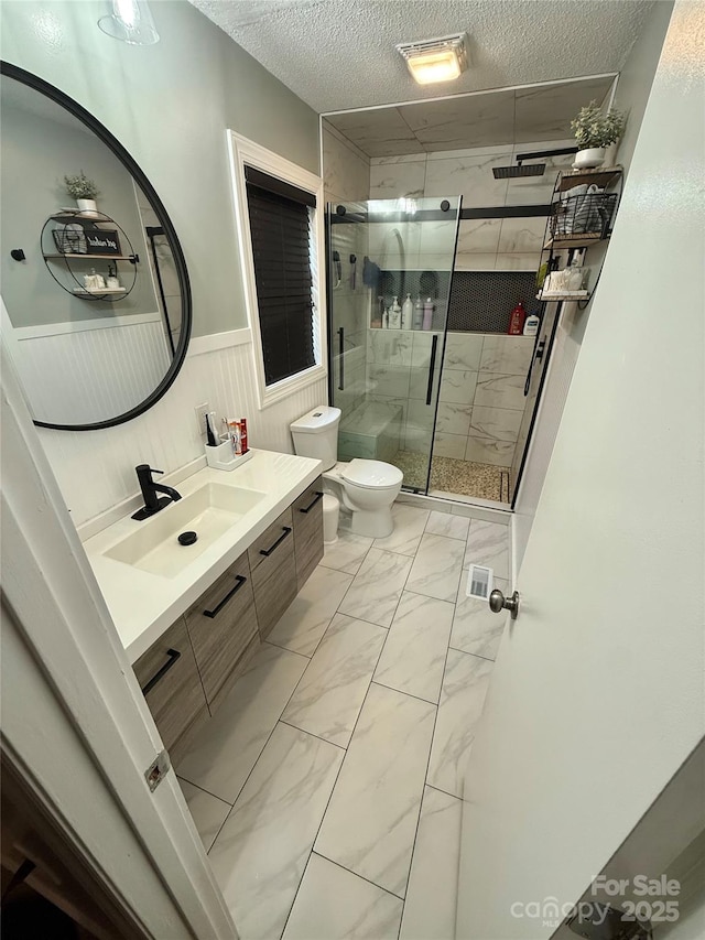 bathroom with marble finish floor, toilet, vanity, wainscoting, and a textured ceiling