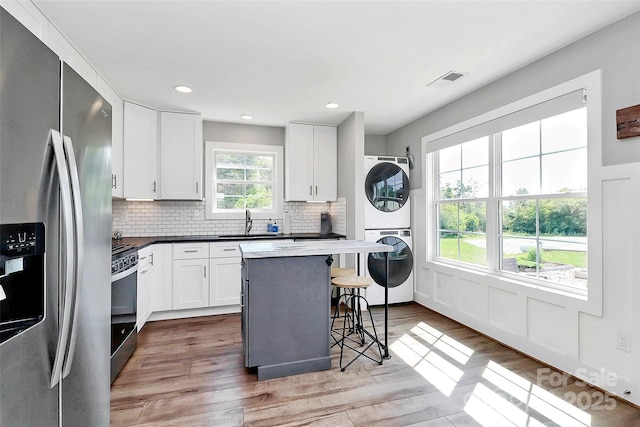 kitchen with stacked washer and dryer, stove, a kitchen breakfast bar, stainless steel fridge, and a sink