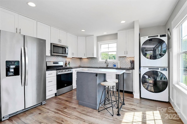 kitchen featuring a kitchen island, stacked washer / dryer, a breakfast bar, a sink, and stainless steel appliances