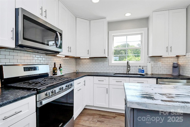 kitchen with a sink, appliances with stainless steel finishes, white cabinets, and light wood-style floors