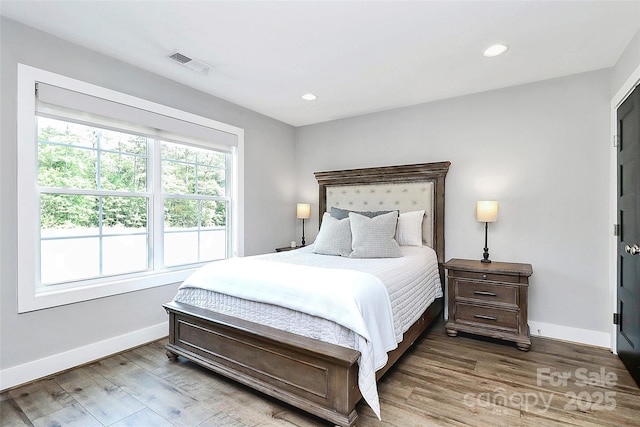 bedroom with baseboards, visible vents, and wood finished floors