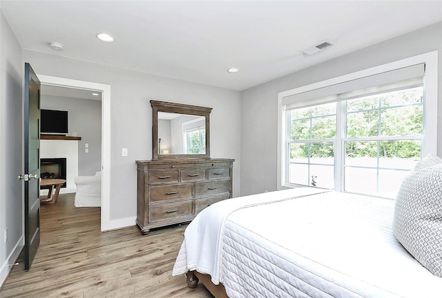 bedroom with a fireplace, recessed lighting, baseboards, light wood-type flooring, and visible vents