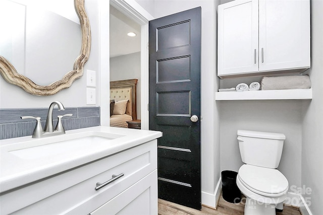 bathroom with toilet, recessed lighting, wood finished floors, and vanity