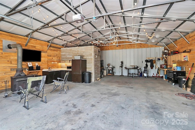 garage featuring a garage door opener, freestanding refrigerator, a wood stove, and wood walls