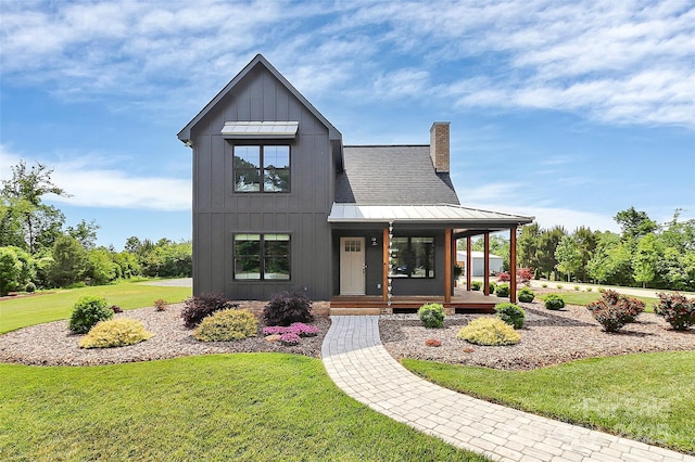 modern farmhouse featuring a standing seam roof, covered porch, a chimney, and a front yard