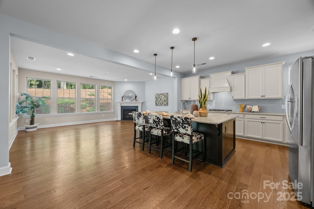 kitchen with open floor plan, white cabinetry, wood finished floors, an island with sink, and appliances with stainless steel finishes