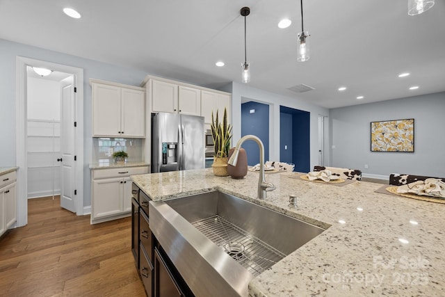 kitchen featuring hanging light fixtures, wood finished floors, a sink, stainless steel fridge, and recessed lighting