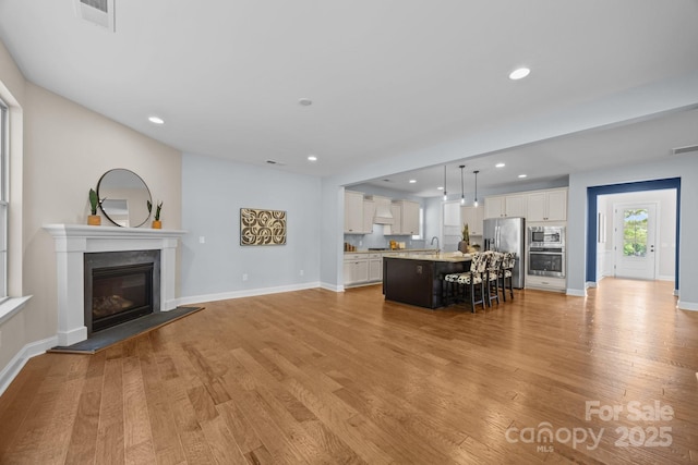 living room featuring a glass covered fireplace, baseboards, recessed lighting, and light wood-style floors