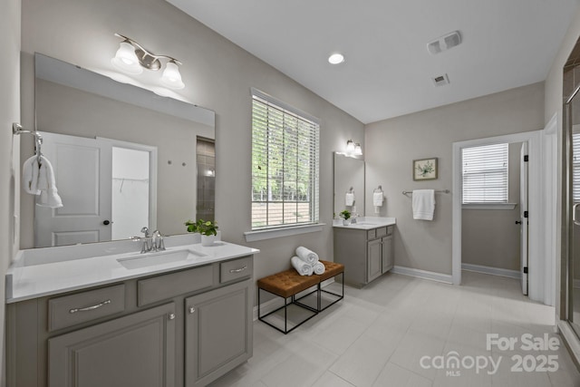 full bath featuring two vanities, a shower stall, baseboards, and a sink