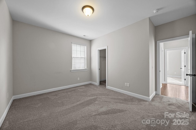 unfurnished bedroom featuring a walk in closet, carpet flooring, and baseboards