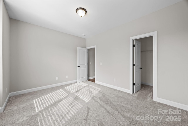 unfurnished bedroom with a walk in closet, baseboards, and light carpet