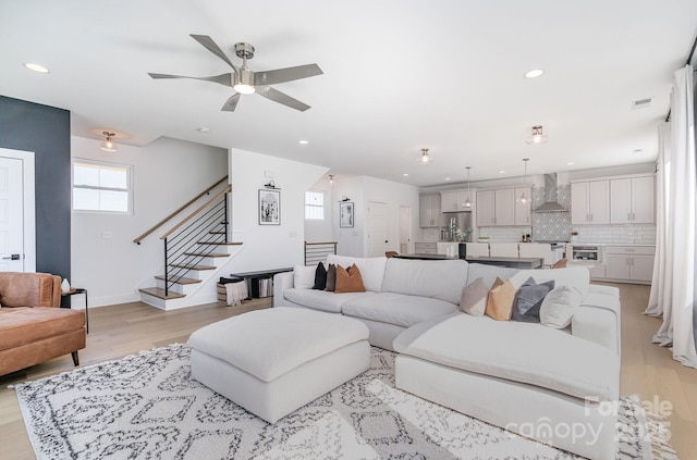 living area with recessed lighting, light wood finished floors, ceiling fan, and stairway
