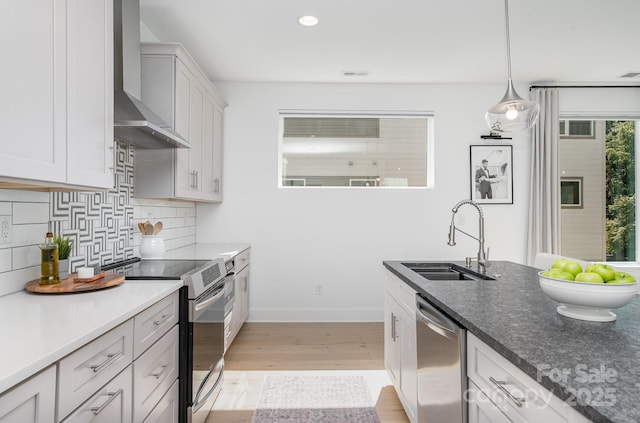 kitchen with wall chimney range hood, tasteful backsplash, a sink, light wood finished floors, and stainless steel appliances