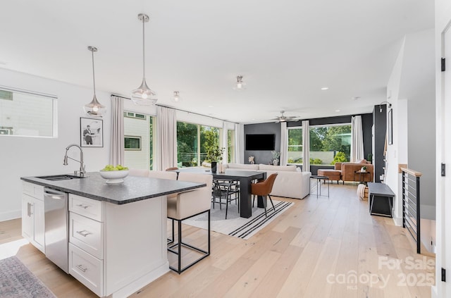 kitchen with white cabinets, dark countertops, a sink, light wood-style flooring, and open floor plan