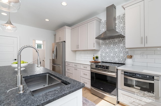 kitchen with wall chimney range hood, recessed lighting, a sink, light wood finished floors, and appliances with stainless steel finishes