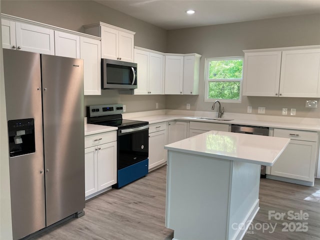 kitchen with light wood finished floors, stainless steel appliances, a sink, white cabinetry, and light countertops