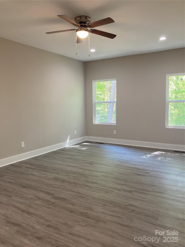 spare room with a ceiling fan, baseboards, a healthy amount of sunlight, and dark wood-type flooring