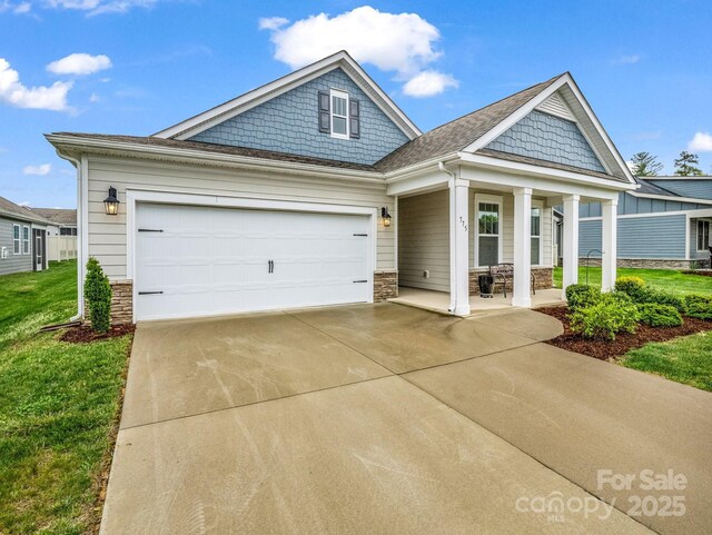 775 Summerfield Pl, Flat Rock, NC 28731 - view of front of house featuring a front lawn, concrete driveway, an attached garage, covered porch, and stone siding