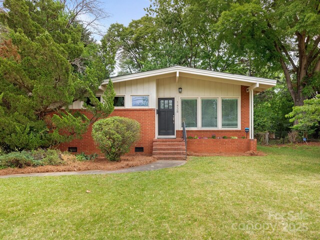 mid-century inspired home with a front lawn, fence, brick siding, entry steps, and crawl space