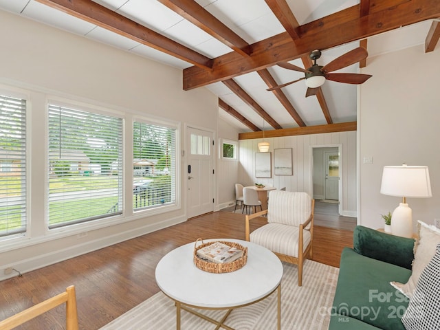 living area featuring plenty of natural light, vaulted ceiling with beams, a ceiling fan, and wood finished floors