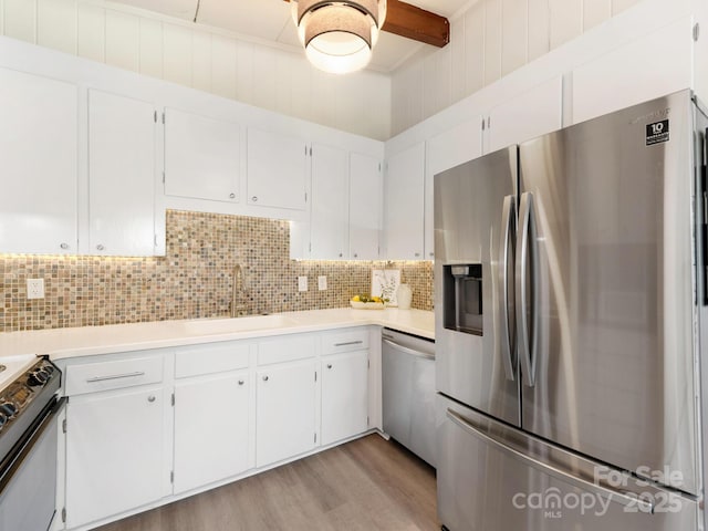 kitchen featuring a sink, decorative backsplash, light wood-type flooring, light countertops, and appliances with stainless steel finishes