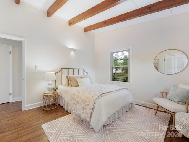 bedroom featuring beamed ceiling, wood finished floors, and baseboards