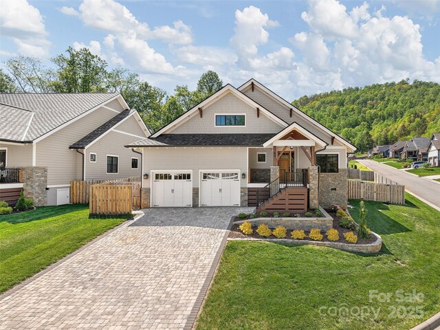 craftsman inspired home featuring an attached garage, decorative driveway, a front lawn, and fence