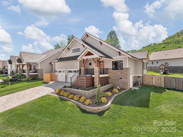 craftsman-style home featuring a front lawn, fence, stone siding, cooling unit, and decorative driveway