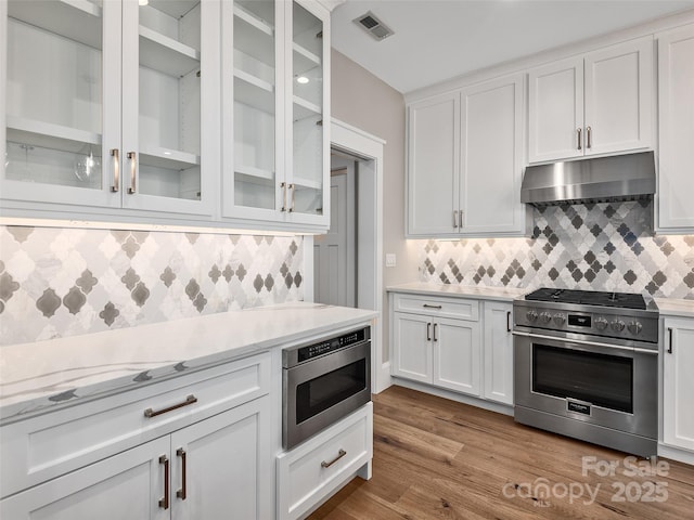 kitchen featuring under cabinet range hood, backsplash, visible vents, and high end stainless steel range oven