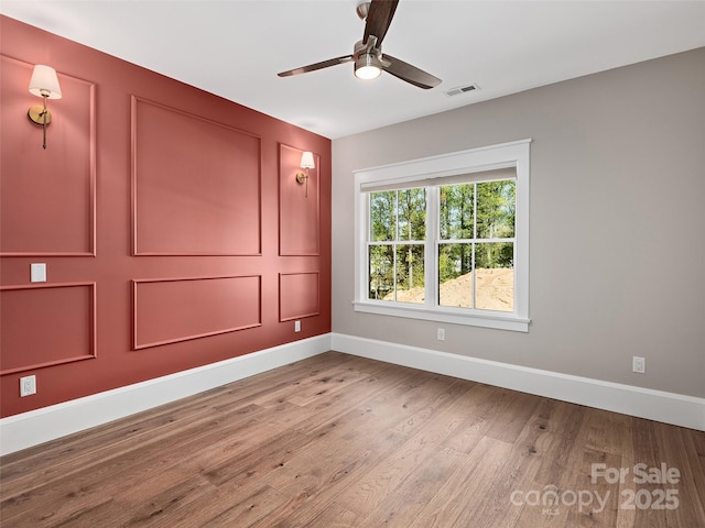 spare room with ceiling fan, baseboards, visible vents, and wood finished floors