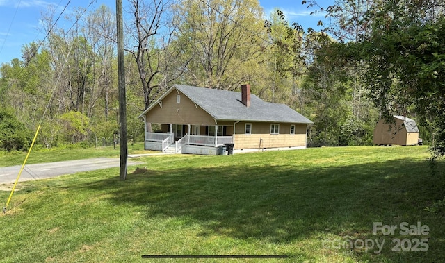 view of front of home with covered porch, a chimney, a front yard, an outdoor structure, and a storage unit