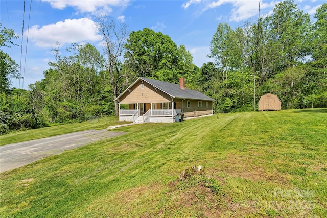 view of front of house featuring an outdoor structure, a storage shed, a front yard, a chimney, and covered porch