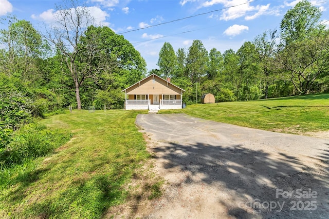 bungalow-style house with covered porch, aphalt driveway, an outbuilding, a storage unit, and a front lawn