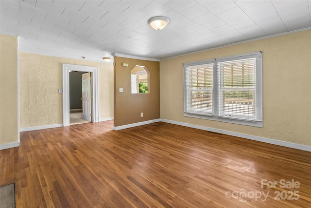 empty room featuring visible vents, ornamental molding, a textured wall, baseboards, and hardwood / wood-style flooring