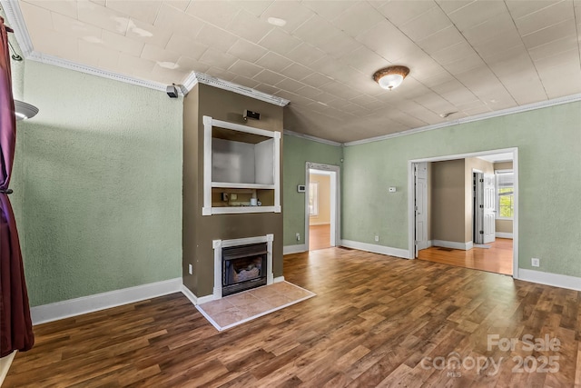 unfurnished living room with crown molding, a fireplace with raised hearth, a textured wall, and wood finished floors