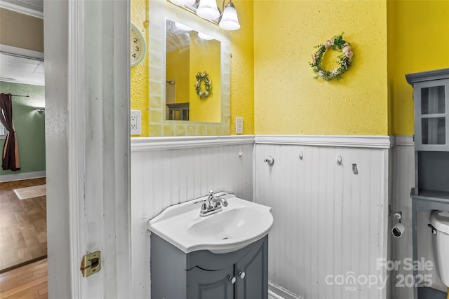 bathroom featuring a textured wall, wainscoting, wood finished floors, and vanity