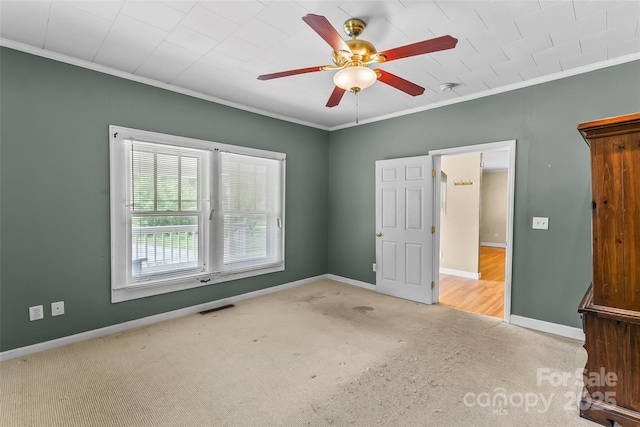 carpeted empty room featuring a ceiling fan, baseboards, visible vents, and ornamental molding