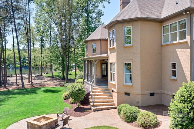 exterior space with a chimney, a shingled roof, a yard, a fire pit, and stucco siding