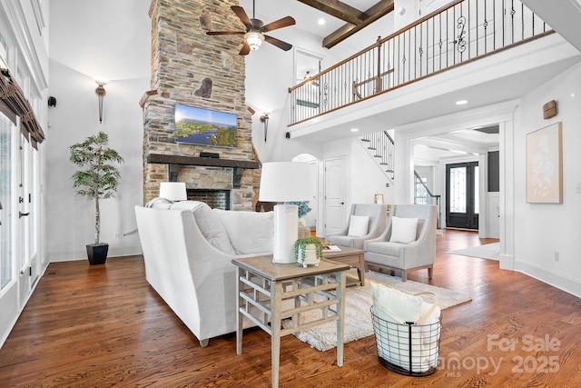 living area with a towering ceiling, wood finished floors, a stone fireplace, baseboards, and a ceiling fan