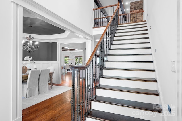 stairway featuring crown molding, an inviting chandelier, wainscoting, a decorative wall, and wood finished floors