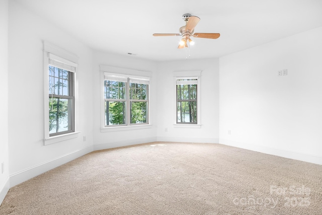 carpeted spare room with a ceiling fan, baseboards, visible vents, and plenty of natural light