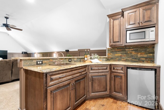 kitchen featuring fridge, a sink, stainless steel microwave, tasteful backsplash, and vaulted ceiling