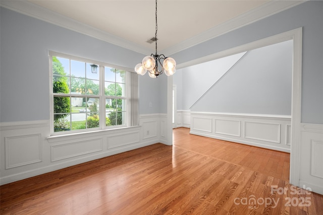 unfurnished dining area with crown molding, an inviting chandelier, wainscoting, light wood-style floors, and visible vents