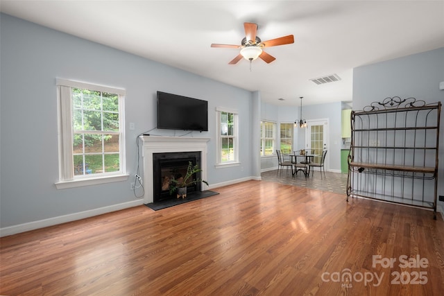 living area featuring visible vents, wood finished floors, a fireplace, baseboards, and ceiling fan with notable chandelier