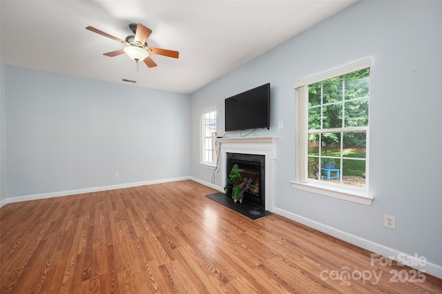 unfurnished living room featuring visible vents, wood finished floors, baseboards, a fireplace with raised hearth, and a ceiling fan