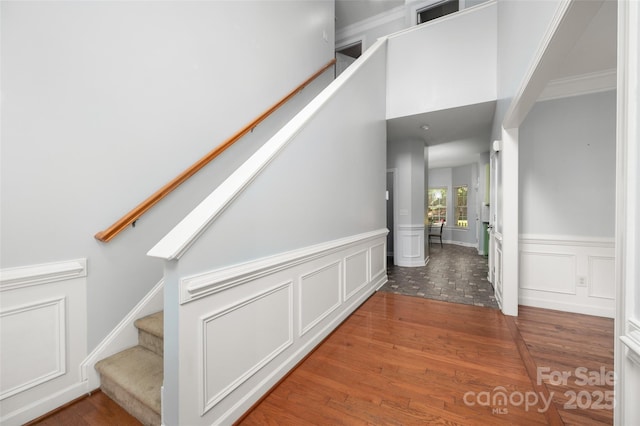 corridor with wood finished floors, stairs, a decorative wall, and wainscoting
