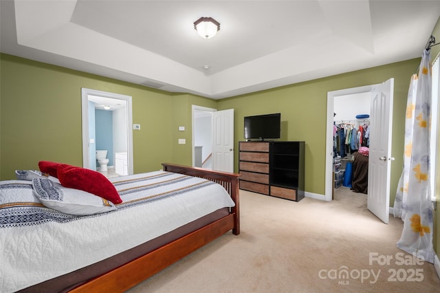 bedroom with a walk in closet, a raised ceiling, a closet, ensuite bathroom, and light carpet